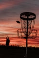 A silhouette of a man throwing a frisbee at a frisbee golf
