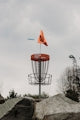 Disc golf basket with a flying disc and orange flag