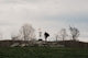 Man walking towards a disc golf basket on a hill.